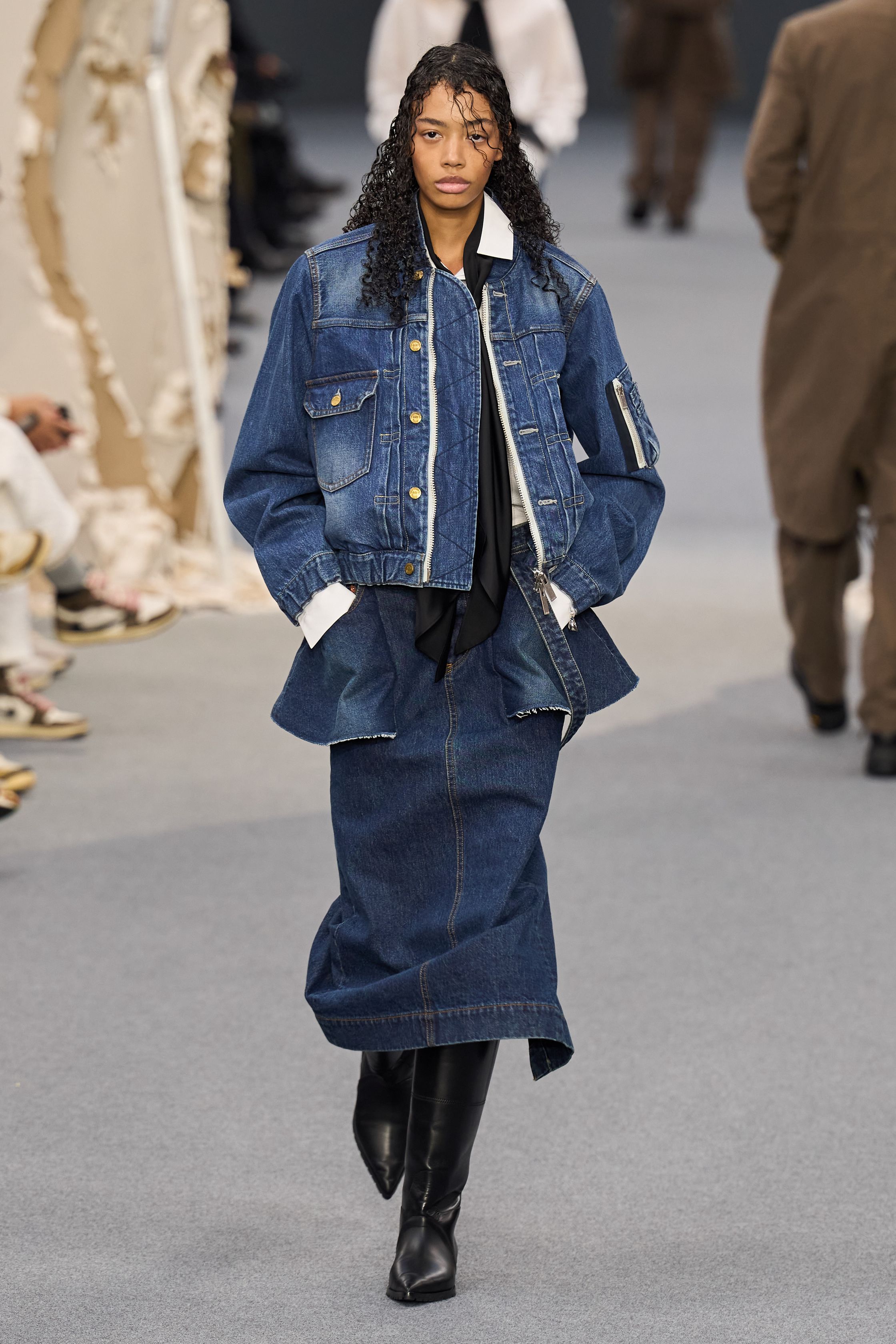 Sacai 2026秋冬再次展示其无可复制的“混合美学”。正装、牛仔、皮草与制服元素被高度结构化地拼接，形成既熟悉又陌生的服装形态。性别边界被进一步模糊，层叠结构制造流动节奏，使行走本身成为设计的一部分。系列在秩序与混乱之间找到平衡，是Sacai 对当代复杂生活状态的持续回应-顽石频道趋势研究